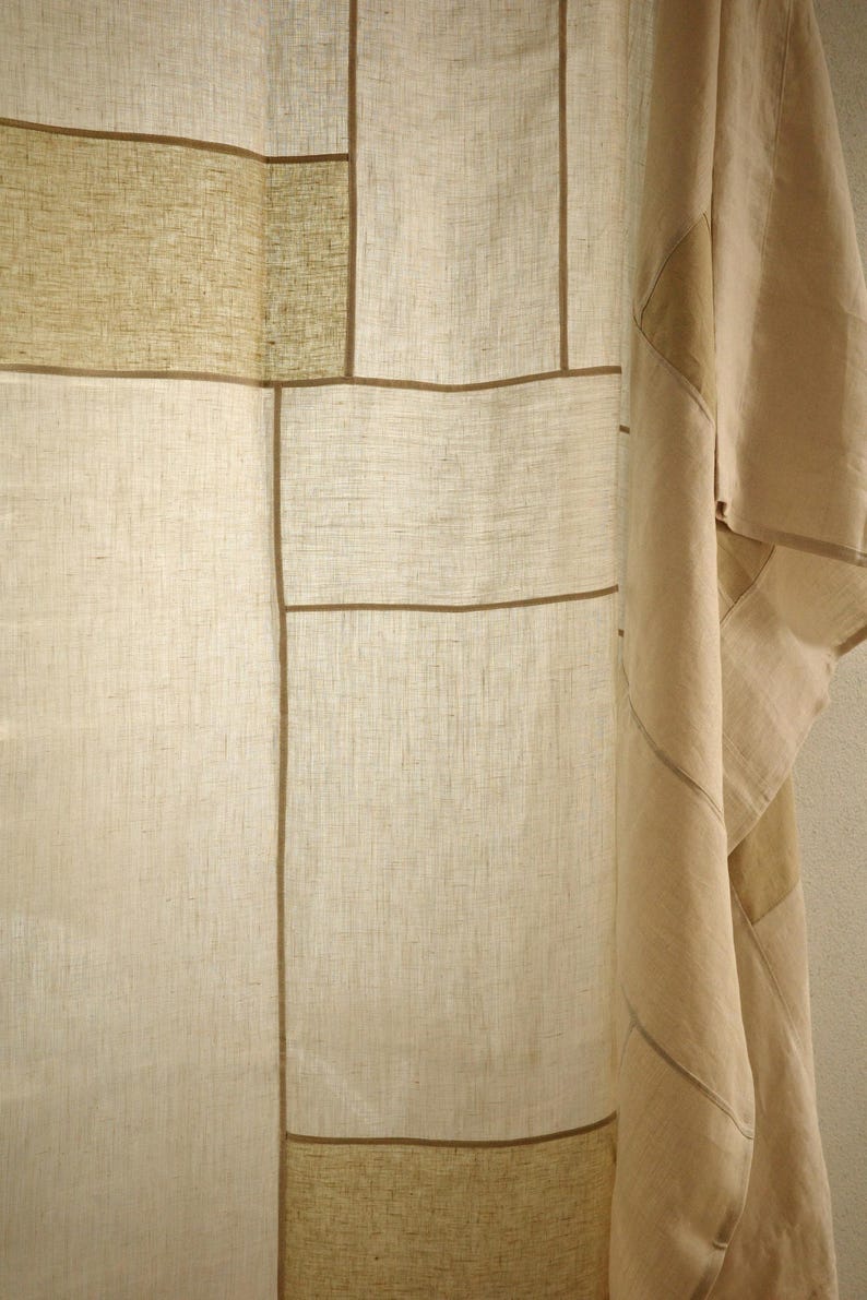 Puede incluir: Una cortina de color beige y bronceado claro con un dise&ntilde;o de patchwork tipo cuadr&iacute;cula y textura de tela visible. El panel est&aacute; construido con secciones rectangulares de material tipo lino separadas por ribetes lineales marr&oacute;n oscuro.