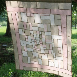 Può includere: Un arazzo tessile rettangolare caratterizzato da un design geometrico patchwork composto da rettangoli di varie dimensioni in tonalità beige, bianco e rosa tenue. I pezzi di tessuto sono uniti da sottili linee marrone scuro a griglia.