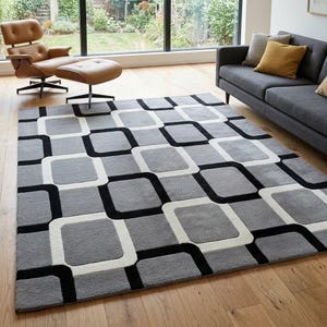May include: A rectangular area rug featuring a repeating geometric pattern of rounded squares in shades of grey, white, and black. The design consists of alternating grey squares outlined by thick white and black borders, creating a grid-like visual effect.