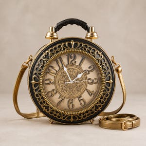 May include: A round handbag shaped like an alarm clock with a gold and black finish. The face features large black numerals, ornate gold filigree detailing, and white clock hands. It includes a top handle, two gold bells, and a detachable shoulder strap.