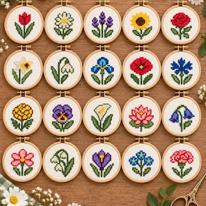 Op de afbeelding: Twintig ronde houten borduurringen met witte stof voorzien van individuele kruissteek bloemmotieven. Elke ring bevat een uniek botanisch patroon, waaronder tulpen, zonnebloemen, rozen en madeliefjes, gerangschikt in een raster op een houten ondergrond.
