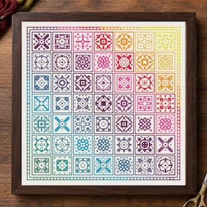 May include: A framed cross-stitch sampler featuring a grid of forty-nine individual square patterns arranged in a rainbow color gradient. Each square contains a unique geometric design stitched in shades of purple, blue, teal, pink, red, orange, and yellow, all enclosed within a dark brown wooden frame.