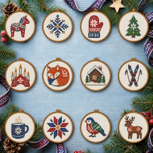 Op de afbeelding: Twaalf ronde houten borduurringen met kruissteekpatronen, waaronder een rood Dala-paardje, een blauwe sneeuwvlok, een rode want, een groene kerstboom, een kandelaar, een oranje vos, een blokhut, ski's, een blauwe mok, een ster, een vogel en een bruin rendier.