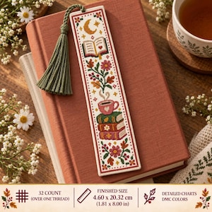 Può includere: Un segnalibro rettangolare a punto croce con una luna crescente, un libro aperto, una tazza rosa e una pila di tre libri, circondati da motivi floreali. Include una nappa verde salvia e misura 4,60 per 20,32 cm come indicato.