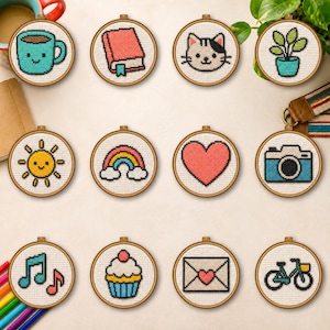 Puede incluir: Una colección de doce bastidores de madera circulares con diseños de punto de cruz que incluyen una taza turquesa, un libro rojo, una cara de gato, una planta en maceta, un sol amarillo, un arcoíris, un corazón rosa, una cámara y una bicicleta.