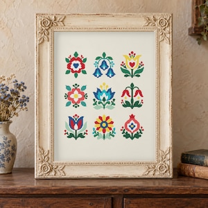 Peut inclure: Un motif de point de croix encadré présentant une grille de neuf motifs floraux distincts aux couleurs vives rouge, bleu, jaune et vert. L'œuvre est présentée dans un cadre rectangulaire orné de couleur crème avec des détails de roses sculptées.