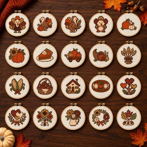 May include: A collection of twenty circular embroidery hoops featuring cross-stitch designs with autumn themes, including turkeys, pumpkins, corn, sunflowers, a house, a pie, a cornucopia, a basket of apples, and floral arrangements on white fabric.