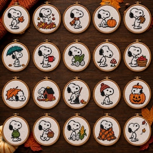May include: A collection of twenty circular wooden embroidery hoops featuring cross-stitch designs of the character Snoopy in various autumn-themed scenes, including pumpkins, falling leaves, cozy blankets, and seasonal harvest items on white fabric.