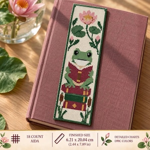 May include: A rectangular cross-stitch bookmark featuring a green frog reading a red book while sitting on a stack of two books. The design includes pink lotus flowers, green lily pads, and cattails on a white background. Finished size 2.44 x 7.89 inches.