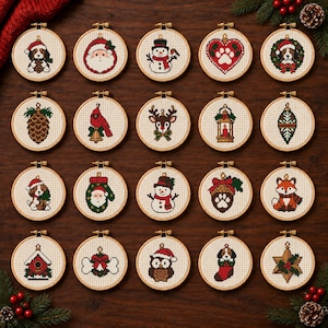 May include: Twenty circular wooden embroidery hoops containing cross-stitch patterns with holiday themes, including a puppy, Santa Claus, snowman, paw print, pinecone, cardinal, reindeer, lantern, fox, owl, birdhouse, and star on white fabric.