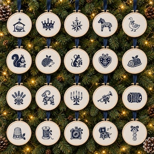 May include: A collection of twenty circular wooden embroidery hoops featuring navy blue cross-stitch designs on white fabric. Each hoop is suspended by a navy blue ribbon and displays unique motifs including animals, holiday symbols, and objects.