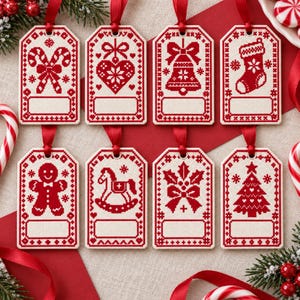 Op de afbeelding: Een set van acht rechthoekige cadeaulabels met rode kruissteekpatronen op een crèmekleurige achtergrond. Elk label toont een uniek kersticoon, waaronder zuurstokken, een hart, een bel, een kerstsok, een peperkoekmannetje, een hobbelpaard, hulst en een kerstboom.