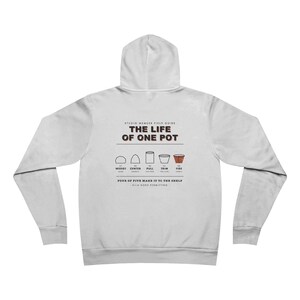 May include: A light gray hooded sweatshirt featuring a back graphic titled The Life of One Pot. The design illustrates five pottery stages: Wedge, Center, Pull, Trim, and Fire, with text stating Four of Five Make It to the Shelf, Kiln Gods Permitting.
