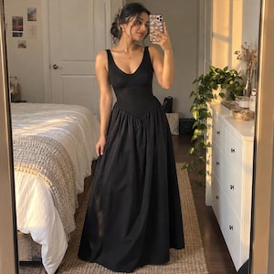 May include: A floor-length black dress featuring a sleeveless bodice with a scoop neckline and a fitted waistline that transitions into a full, flowing skirt. The garment is constructed with a structured, solid-colored fabric.