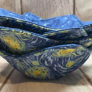 May include: A stack of four blue fabric bowls. The bowls are decorated with a print inspired by Van Gogh's "Starry Night" painting, featuring swirling brushstrokes and yellow accents. The bowls are nested together.