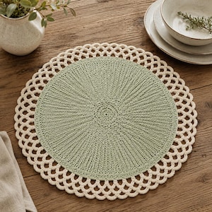 May include: A round crochet placemat featuring a solid sage green centre with a textured, radiating stitch pattern, surrounded by a wide, cream-coloured border with an intricate, openwork scalloped edge design that creates a delicate lace effect.