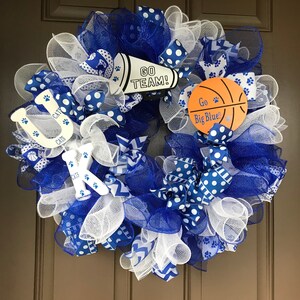 May include: A blue and white wreath with a basketball, a megaphone, and the letters "UK" with the word "CATS" on each letter. The megaphone says "GO TEAM!" and the basketball says "Go Big Blue!"