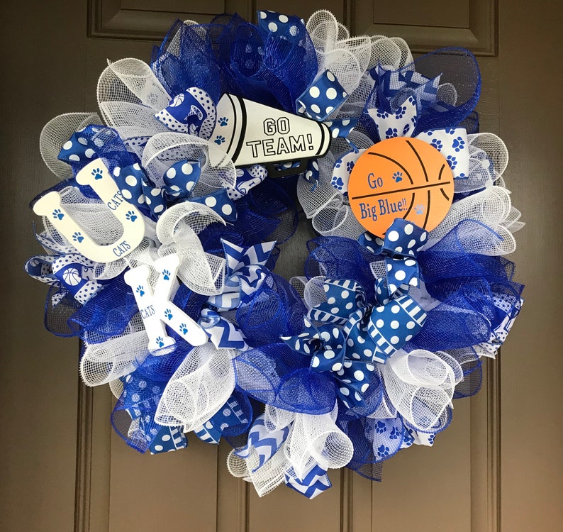 May include: A blue and white wreath with a basketball, a megaphone, and the letters "UK" with the word "CATS" on each letter. The megaphone says "GO TEAM!" and the basketball says "Go Big Blue!"