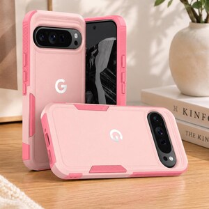 May include: Two light pink protective phone cases for a Google Pixel device. The cases feature a dual-tone design with a darker pink frame, a prominent camera bar cutout, and a white Google G logo centered on the back of the phone case exterior.