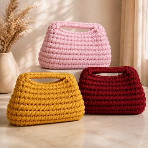 May include: Three rectangular crochet handbags with integrated handles. One bag is light pink, one is mustard yellow, and one is deep burgundy. Each bag features a thick, textured, horizontal stitch pattern and a structured, boxy silhouette.