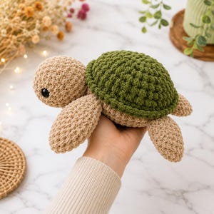 May include: A handmade crochet turtle toy featuring a textured beige head and limbs with a dark green shell. The stuffed animal has small black plastic eyes and is crafted with a visible yarn stitch pattern throughout its entire body structure.