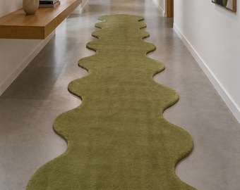 May include: A long, olive green runner rug with a distinct wavy, organic edge design. The rug features a soft, textured pile surface and follows a continuous, irregular scalloped shape that extends along the length of the floor.