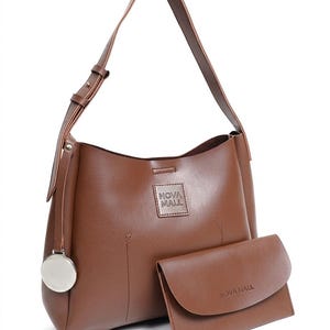 May include: A brown shoulder bag with a single adjustable strap and a matching rectangular clutch. The bag features a square patch with the text NOVA MALL and a circular silver metal charm. The clutch also displays the text NOVA MALL on its front flap.