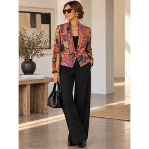May include: A long-sleeve blazer featuring an abstract multicolored print in shades of orange, purple, and yellow, worn over a black top and black wide-leg trousers. The outfit is paired with a black handbag and dark-tinted sunglasses.