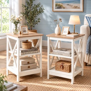 May include: Two square side tables with white wooden frames and light brown wood-grain tops. Each table features an X-shaped side design, a middle shelf, and a bottom shelf. The tables are styled with books, small baskets, and picture frames.