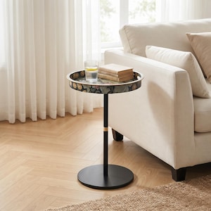 May include: A round side table with a black metal pedestal base and a circular tray top featuring a dark floral pattern. The table holds a clear glass of water and a small stack of two beige books on its surface.