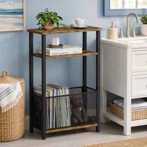 May include: A tall, narrow storage shelf with a black metal frame and two rustic brown wood-grain shelves. The top shelf holds a potted green plant and a white cup. The middle shelf holds a book titled Deep Roots. The bottom is a black metal mesh bin.