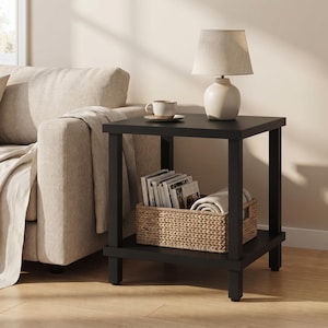 May include: A square black side table with four legs and a lower shelf. The top surface holds a beige table lamp and a ceramic mug on a saucer. A woven basket containing magazines and a folded white textile sits on the lower shelf.