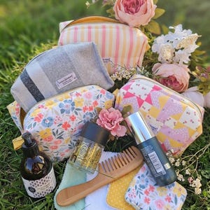 Peut inclure: Quatre trousses zippées en tissu à motifs rayés, écossais gris, floraux et géométriques jaune et rose. L'ensemble comprend un flacon pompe ambré, un pot transparent à paillettes dorées, un peigne en bois et trois carrés de tissu fleuris et jaunes.