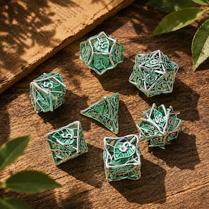 May include: A set of seven polyhedral dice featuring a silver metal cage design with intricate leaf patterns and a vibrant green enamel inlay. Each die displays clear, embossed numbers, including a twenty-sided die, a twelve-sided die, and others.
