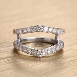 May include: A silver-toned double chevron ring guard featuring two V-shaped bands connected by vertical bars. Both bands are encrusted with alternating round and princess-cut clear stones. The text LabdiamondTreasures is visible on the band.