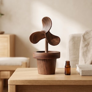 May include: A dark brown wooden sculpture shaped like a flower in a pot, featuring three curved petals on a central stem, accompanied by a small amber glass bottle with a black cap, both resting on a light-colored wooden surface.