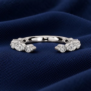 May include: A silver-toned open ring featuring a series of alternating round and marquise-cut clear stones set along the band. The ring has a gap at the front, showcasing a polished metal finish and faceted stones that catch the light.