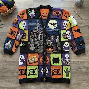 May include: A long-sleeved crochet cardigan featuring a patchwork design with Halloween motifs including a witch, a haunted house, skulls, pumpkins, ghosts, spiders, and the text "Boo!". The garment has a black button placket with skull-shaped buttons.
