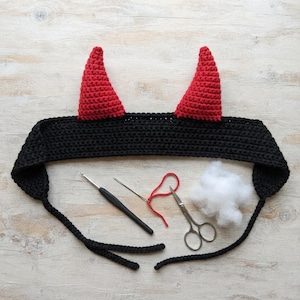 Può includere: Una fascia all'uncinetto nera con due corna da diavolo rosse a punta. Il set include un uncinetto nero, un ago da cucito argentato con un filo rosso, un paio di forbici argentate e un piccolo ciuffo di imbottitura in fibra bianca.