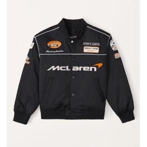 Può includere: Una giacca nera con bottoni che presenta il logo McLaren in bianco e arancione sul petto. Il capo include varie toppe a tema automobilistico, tra cui una grafica McLaren F1, la scritta Formula Racing e profili bianchi lungo le spalle.
