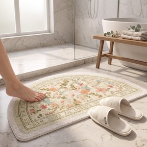 May include: A semi-circular bath mat featuring a cream-colored background with a floral pattern in shades of pink, blue, and green. The border contains the text "PLEASE ACCEPT MY BEST WISHES FOR YOUR SUCCESS". A pair of beige slippers sits nearby.