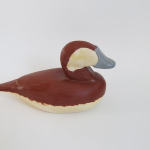 May include: A hand-carved wooden duck decoy with a brown body, white underbelly, and a gray beak. The decoy is painted in a realistic style.