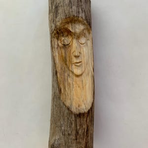 May include: A wooden sculpture of a face carved into a piece of driftwood. The face has closed eyes and a serene expression.