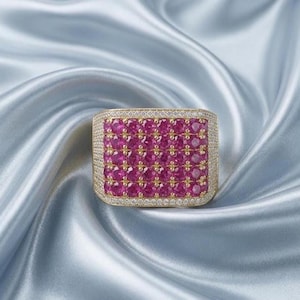 May include: A rectangular gold ring featuring a grid of vibrant pink round-cut stones set in the center. The entire surface of the ring, including the border surrounding the pink stones, is encrusted with small, clear white pavé-set crystals.