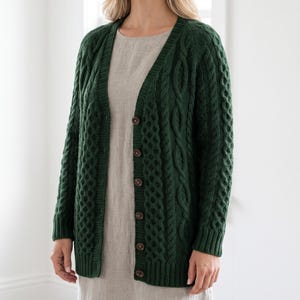 May include: A dark forest green cable-knit cardigan featuring a V-neckline, long sleeves, and a front button closure with five brown buttons. The knit pattern consists of vertical braided cables and textured panels, finished with ribbed cuffs and hem.