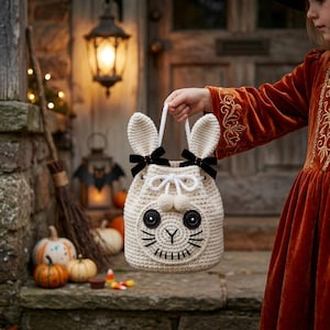 May include: A cream-colored crocheted drawstring bag shaped like a rabbit with long ears, black button eyes, and embroidered whiskers. The bag features two black velvet bows at the base of the ears, a white rope handle, and two small pom-poms.