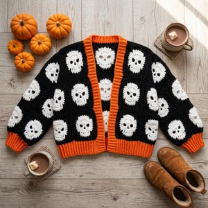 May include: A long-sleeve crochet cardigan featuring a repeating pattern of white skulls on black square panels, finished with vibrant orange ribbed trim along the front opening, cuffs, and bottom hem, constructed from yarn.