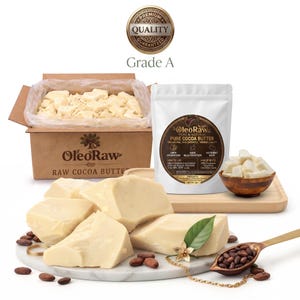 Könnte beinhalten: Ein Pappkarton gefüllt mit cremefarbenen Kakaobutterstücken, ein weißer Beutel mit der Aufschrift OleoRaw Pure & Natural Pure Cocoa Butter und eine Holzschale mit Kakaobutterstücken. Große Kakaobutterstücke liegen auf einer weißen Marmorplatte.