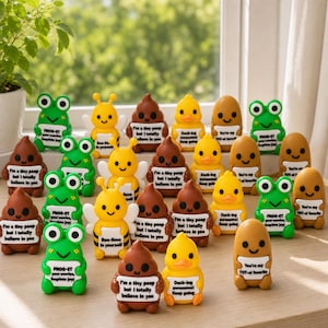 May include: A collection of small, colourful resin figurines featuring frogs, bees, ducks, and brown shapes, each holding a white sign with printed motivational text. The figures are arranged in rows, displaying various expressions and puns.