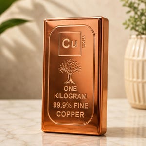 Könnte beinhalten: Ein rechteckiger Kupferbarren mit polierter Oberfläche. Die Vorderseite zeigt das chemische Symbol Cu, ein Baum-Symbol und den Text ONE KILOGRAM 99.9% FINE COPPER. Der Barren hat einen erhabenen Rand und eine kleine Seriennummer oben rechts.